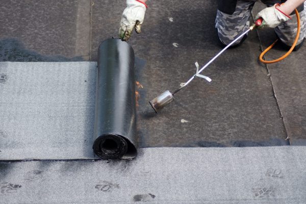 The flat roof installation with propane blowtorch during construction works with roofing felt